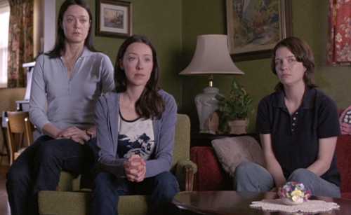 Three women sitting in a living room and listening with sadness and concern to what a fourth person is saying.